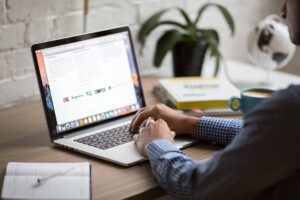 Person working on a laptop at a desk analyzing programmatic ads performance data with a coffee mug and marketing books nearby.