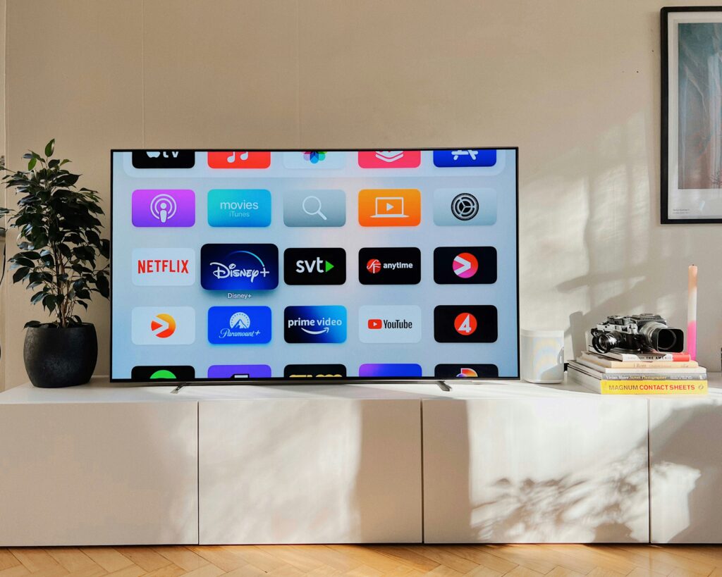 A solid, white TV stand on which stands a smart TV with the Apple TV store and various streaming platforms displayed, like Disney+, Paramount+, and Prime Video. All of these platforms offer CTV inventory.