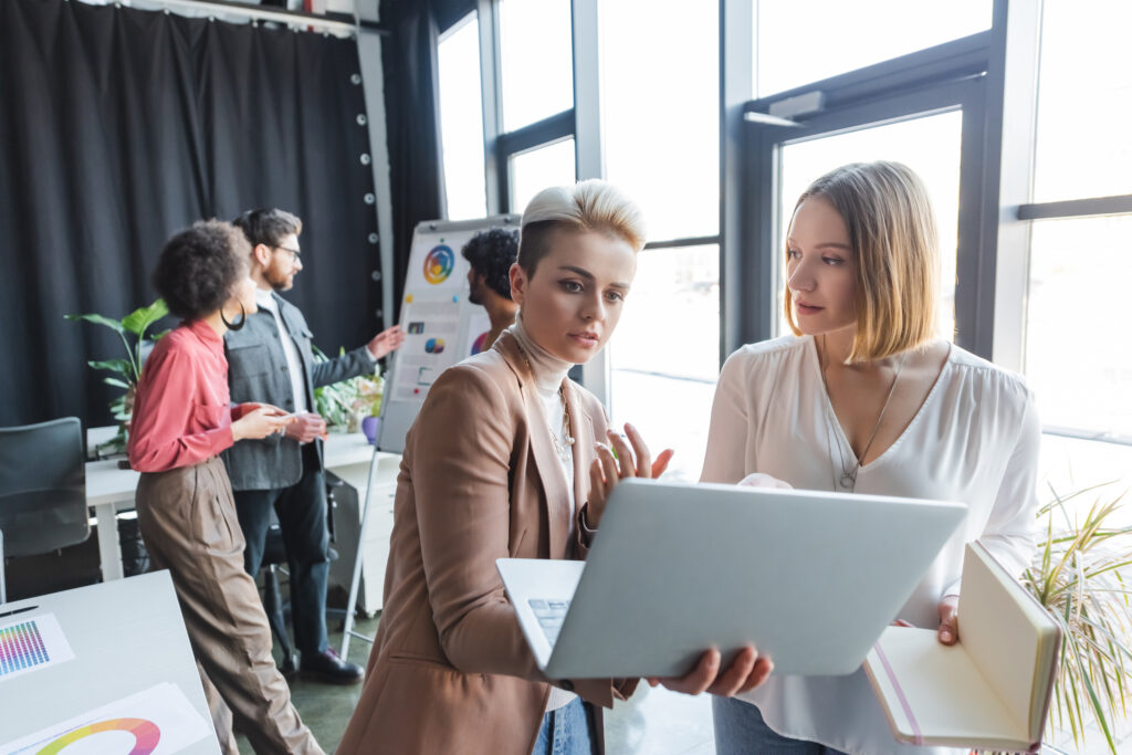advertising managers talking near laptop and multiethnic colleagues near flip chart on background,considering in-housing programmatic