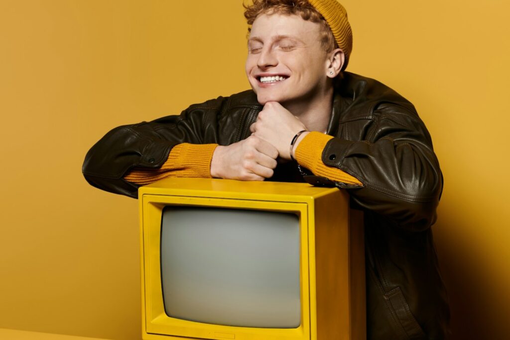Smiling young man leaning on a vintage yellow TV against a yellow backdrop, representing a self-serve DSP and premium CTV advertising theme.